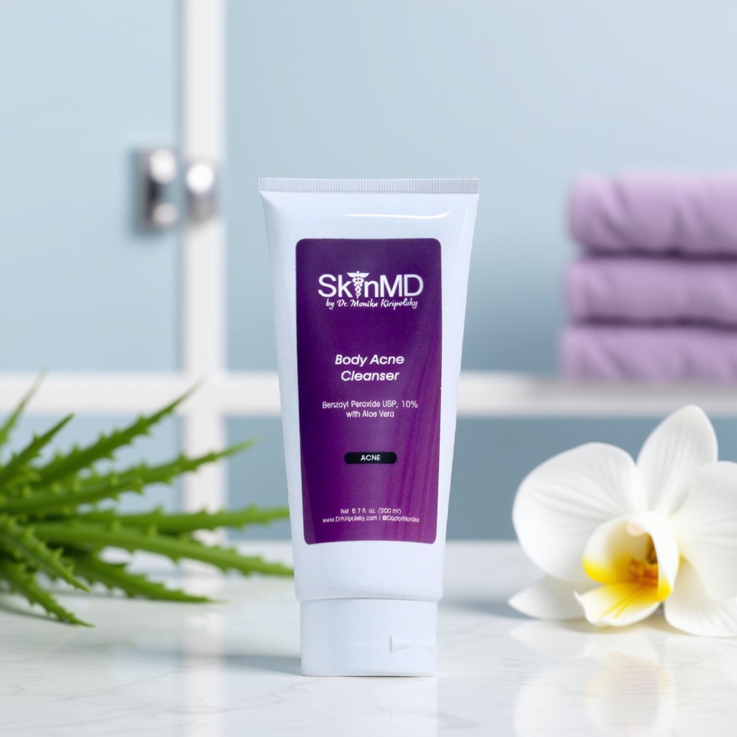 Tube of SkinMD Body Acne Cleanser on a bathroom counter with flowers and towels in the background.